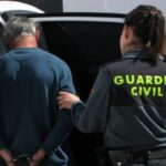 Una guardia civil conduce a un detenido al interior de un vehículo oficial.