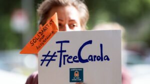 Una manifestante sostiene un cartel con la inscripción "#FreeCarola" en la mano durante una protesta ante el Consulado General de Italia en Colonia en favor de la puesta en libertad de la capitana alemana del barco de rescate de refugiados Sea-W