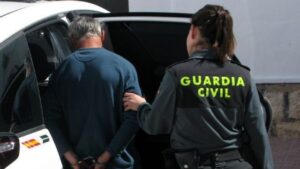 Una guardia civil conduce a un detenido al interior de un vehículo oficial.