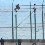 En la imagen, tres de un total de 153 migrantes, entran en Ceuta saltando su doble valla en la primera incursión en grupo en un año.
