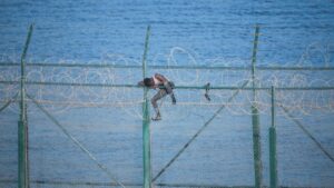 En la imagen, uno de los 153 migrantes, que han entrado en Ceuta saltando su doble valla en la primera incursión en grupo en un año; se aferra a las concertinas