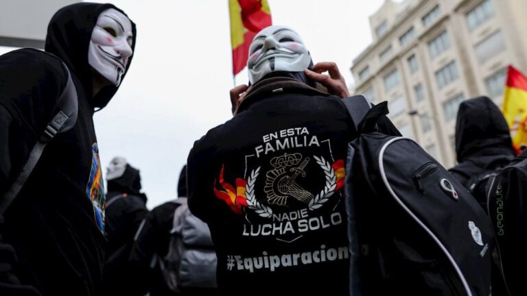 Manifestantes con máscaras de Anonymous y una camiseta en la que reza 'en esta familia nadie lucha solo #equiparación' frente a las puertas del Congreso de los Diputados.