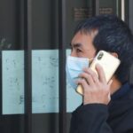 Un hombre de origen asiático pasea con mascarilla por una tienda asiática cerrada como consecuencia del coronavirus, en el barrio de Usera