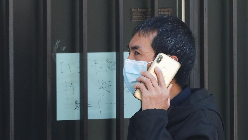 Un hombre de origen asiático pasea con mascarilla por una tienda asiática cerrada como consecuencia del coronavirus, en el barrio de Usera