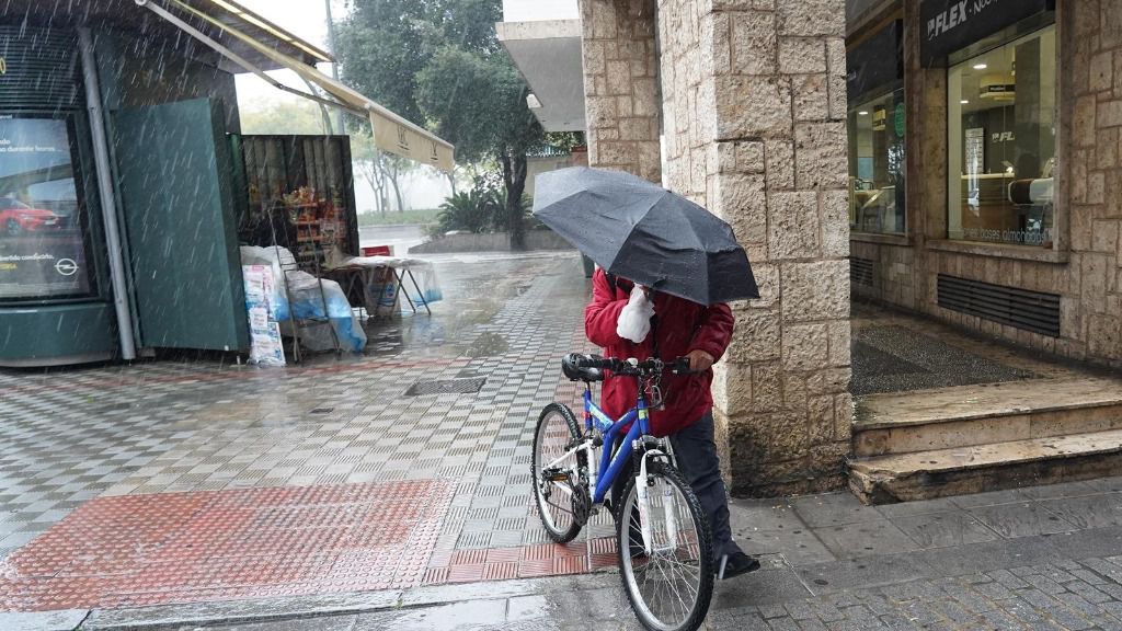Un ciclista con un pagaguas resguardándose de la lluvia y el viento