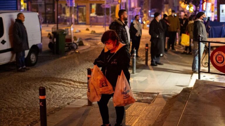 Un mujer ataviada con una mascarilla sale de una tienda de comestibles después de que el Gobierno decretara un toque de queda de 48 horas para el pasado fin de semana y que provocó largas colas en colmados y locales de alimentación