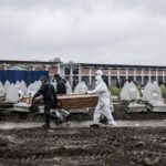 Trabajadores funerarios portan un féretro para enterrarlo en un cementerio en Turín coronavirus