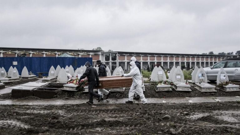 Trabajadores funerarios portan un féretro para enterrarlo en un cementerio en Turín coronavirus