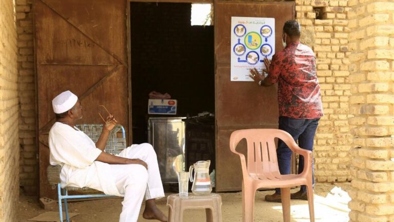 Sudaneses frente a un cartel informativo sobre las medidas de protección ante la pandemia de coronavirus