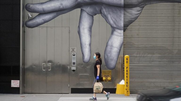Una mujer con mascarilla paseando ante un mural en Nueva York coronavirus