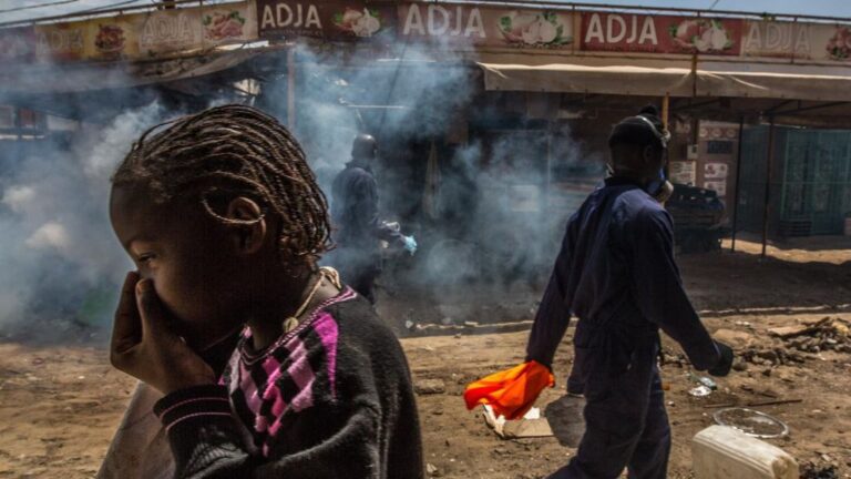 Varias personas caminan por un mercado de Dakar, Senegal, mientras un trabajador desinfecta sus calles
