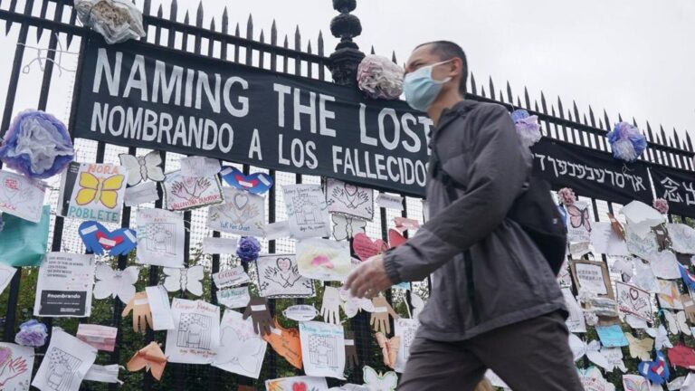 Un hombre pasa ante una verja en Nueva York con mensajes en memoria de los fallecidos por la pandemia del coronavirus