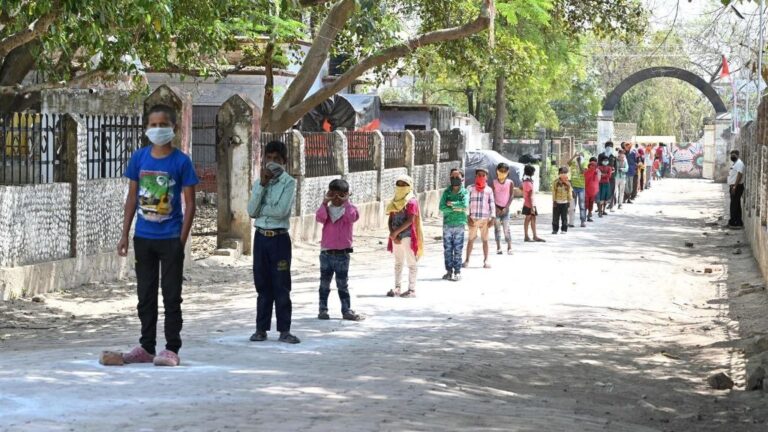 Niños con mascarilla por el coronavirus hacen cola en India para conseguir el menú escolar