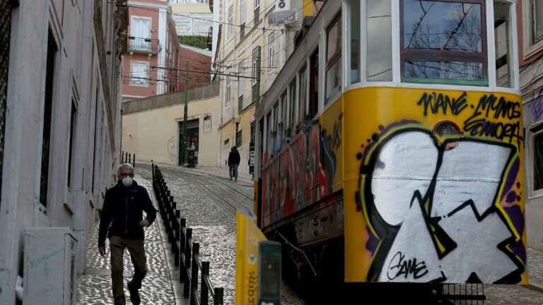 Un hombre con mascarilla junto a un tranvía de Lisboa