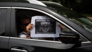 Una trabajadora de Nissan Motor Ibérica, en la Zona Franca de Barcelona, sujeta un papel desde su coche en el que se lee 'Nissan no se cierra'