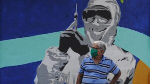 Un hombre con mascarilla ante un mural de un trabajador médico en Bombay coronavirus india