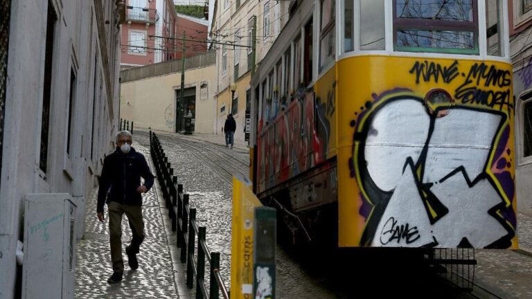 Un hombre con mascarilla junto a un tranvía de Lisboa