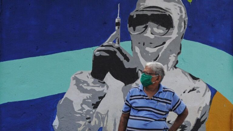 Un hombre con mascarilla ante un mural de un trabajador médico en Bombay coronavirus india