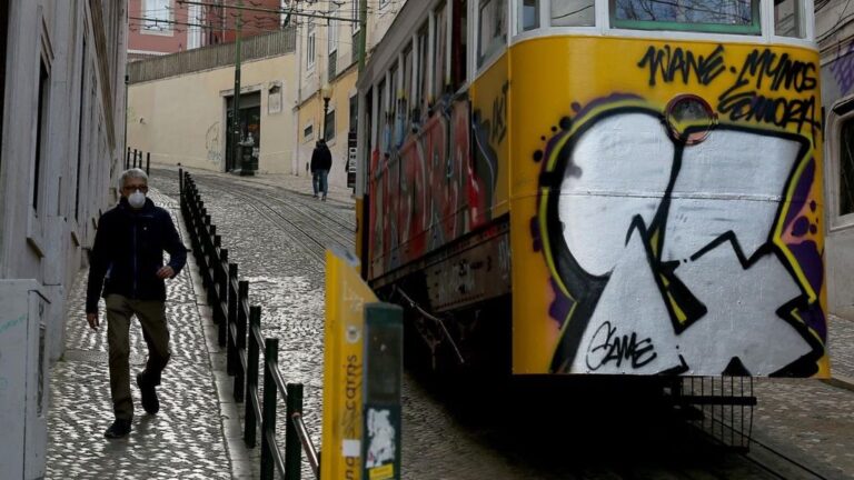 Un hombre con mascarilla junto a un tranvía de Lisboa