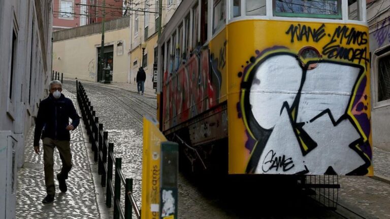 Un hombre con mascarilla junto a un tranvía de Lisboa