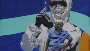 Un hombre con mascarilla ante un mural de un trabajador médico en Bombay coronavirus india