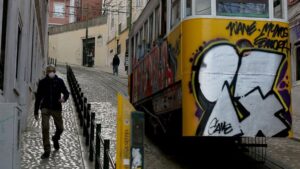 Un hombre con mascarilla junto a un tranvía de Lisboa
