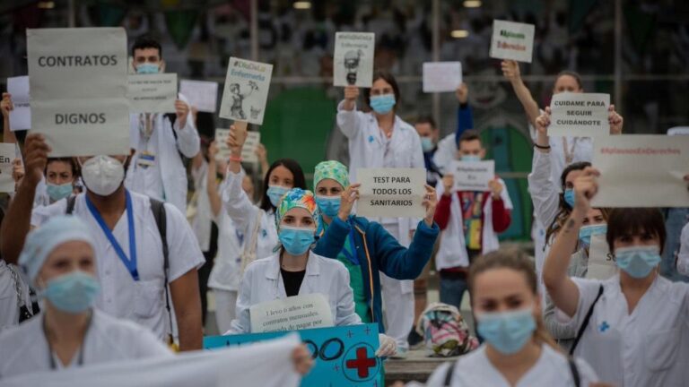 Decenas de miembros del personal sanitario protegidos con mascarilla sostienen carteles durante la concentración de sanitarios en el Día Internacional de la Enfermería a las puertas del Hospital Vall d'Hebron, en Barcelona