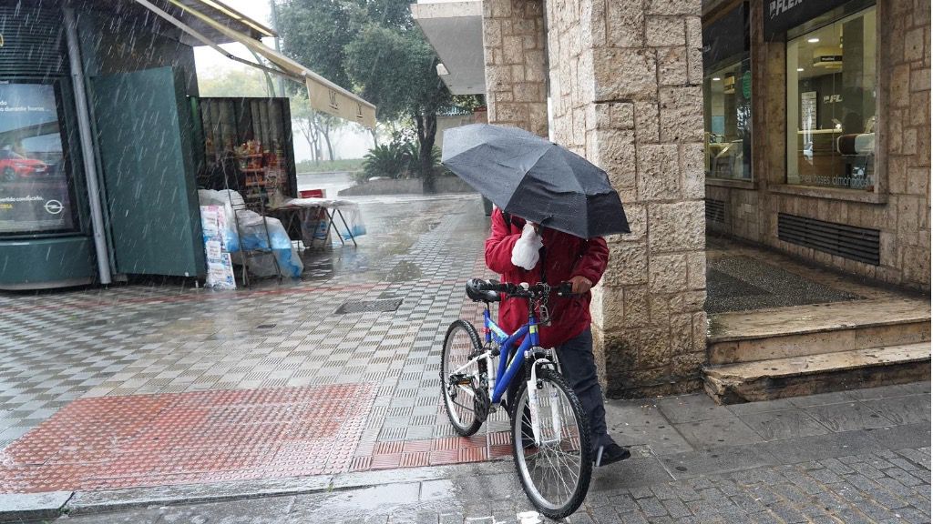 Un ciclista con un pagaguas resguardándose de la lluvia y el viento