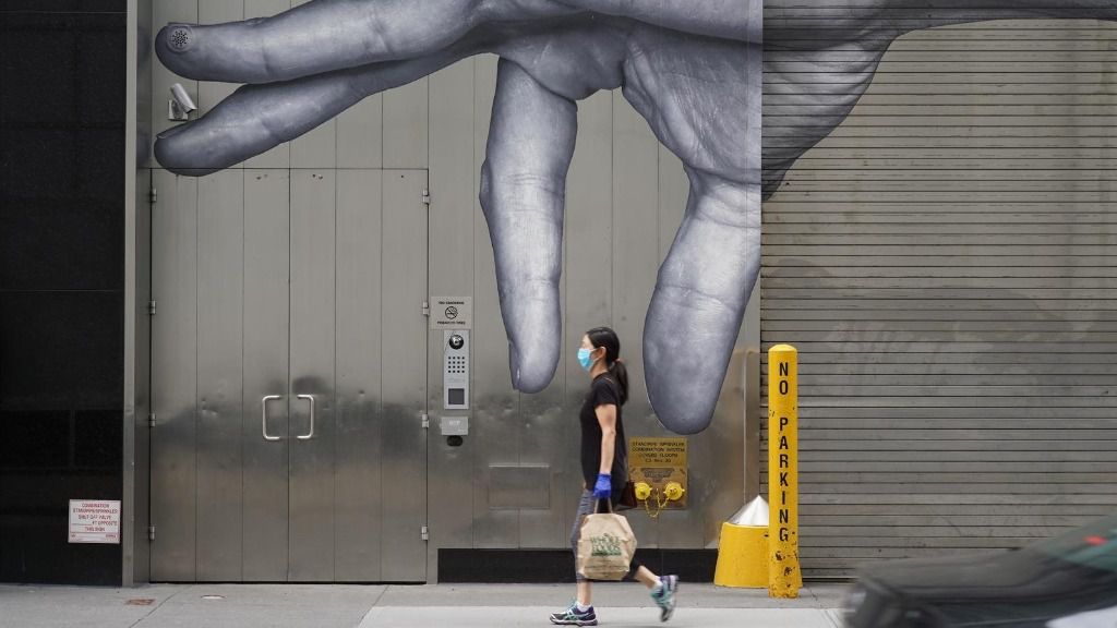 Una mujer con mascarilla paseando ante un mural en Nueva York coronavirus