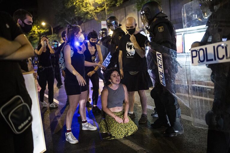 Una joven arrodillada frente a antidisturbios de la Policía Nacional en el barrio de Argüelles