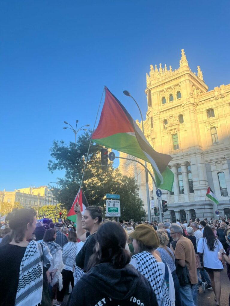 Manifestación con bandera palestina en una plaza concurrida.