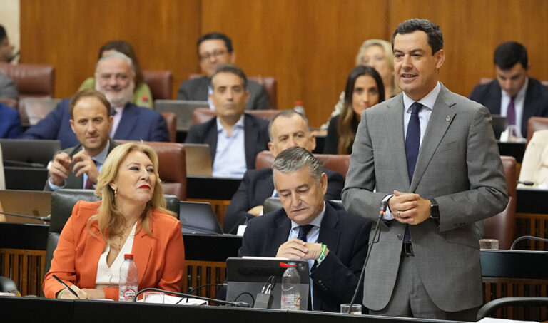 Juan Manuel Moreno hablando en el Parlamento de Andalucía con otros asistentes