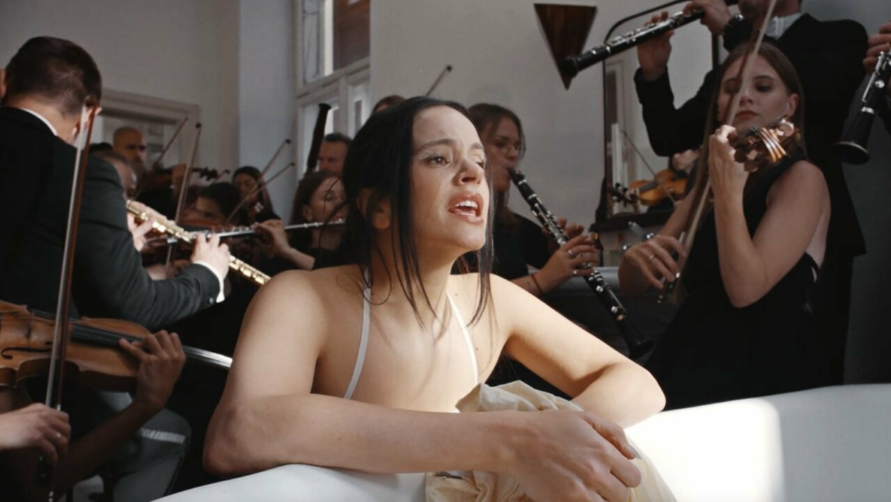 Rosalía interpretando en un entorno orquestal con músicos detrás