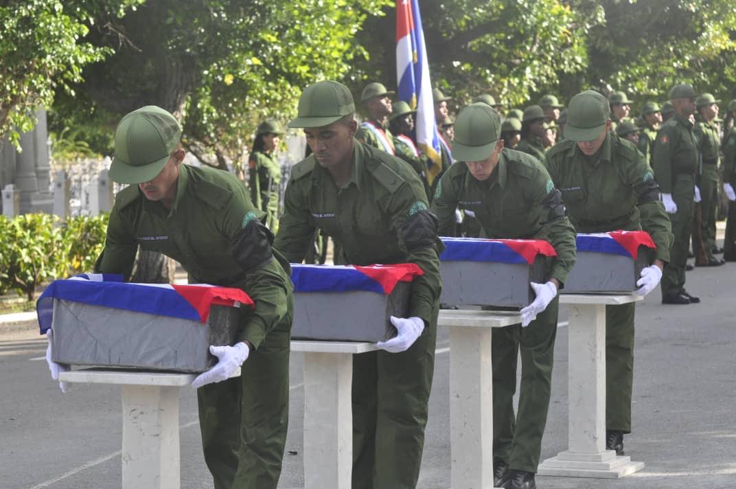 Ceremonia militar con soldados llevando ata&uacute;des cubiertos con banderas.