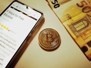 Bitcoin junto a un billete de 50 euros y un smartphone mostrando un art&iacute;culo