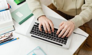 Persona escribiendo en un teclado de laptop rodeada de material de estudio